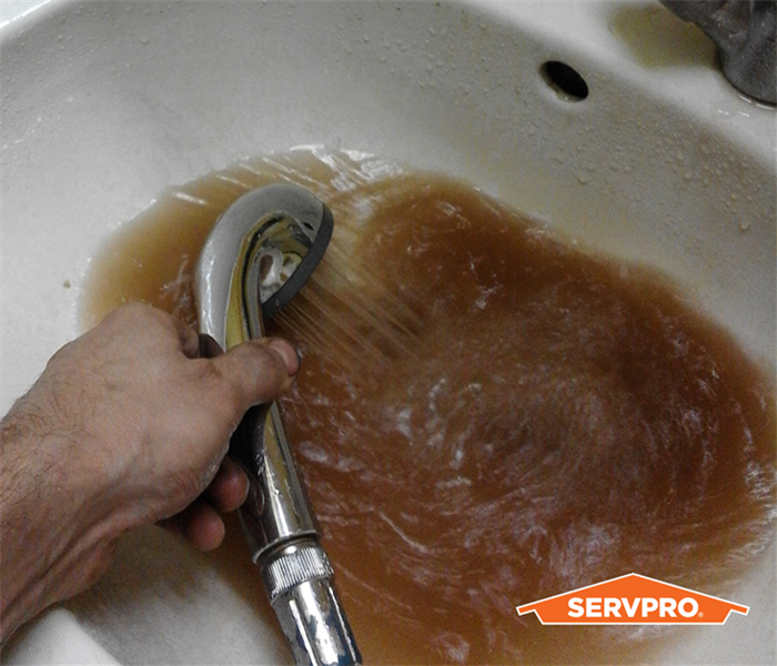 sink full of brown water, man's arm on left holding hose into sink, orange servpro logo, sink is white